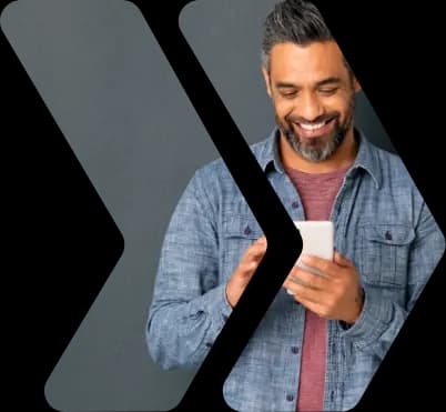 A person leaning against a wall and smiling while interacting with his phone