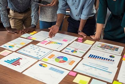 Four people huddled over a table that has pages of charts and graphs laid out.
