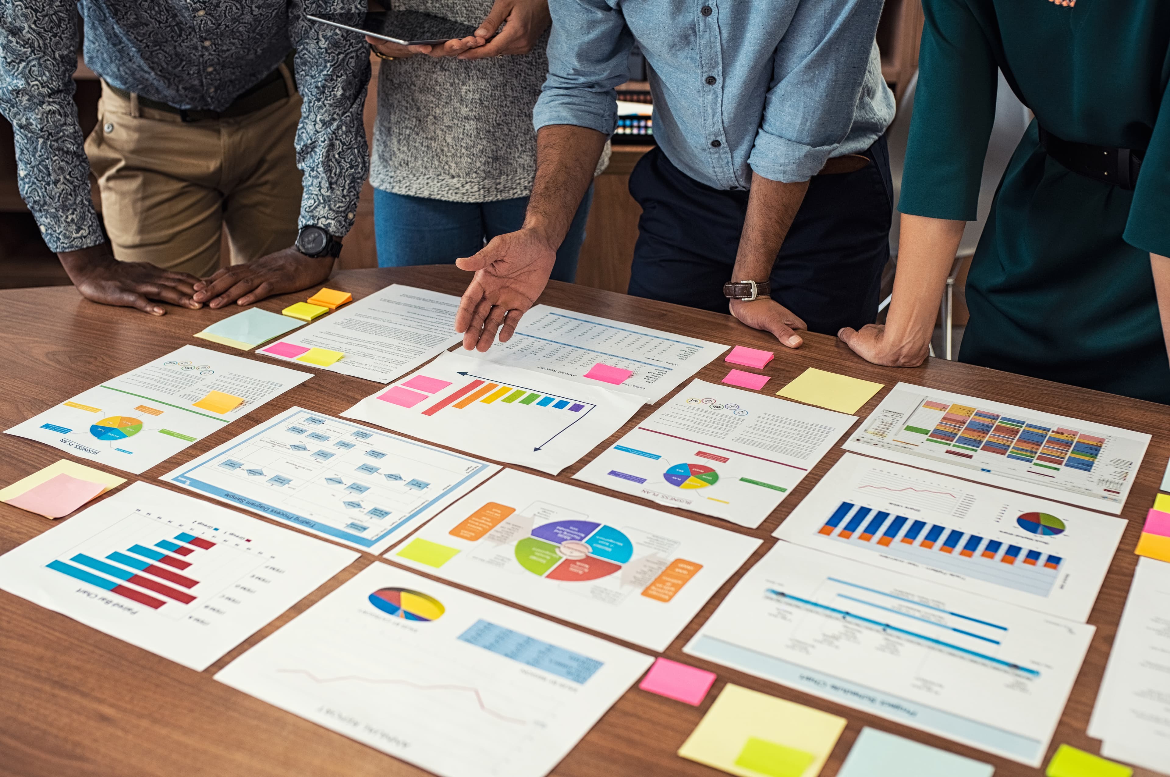 Four people huddled over a table that has pages of charts and graphs laid out.
